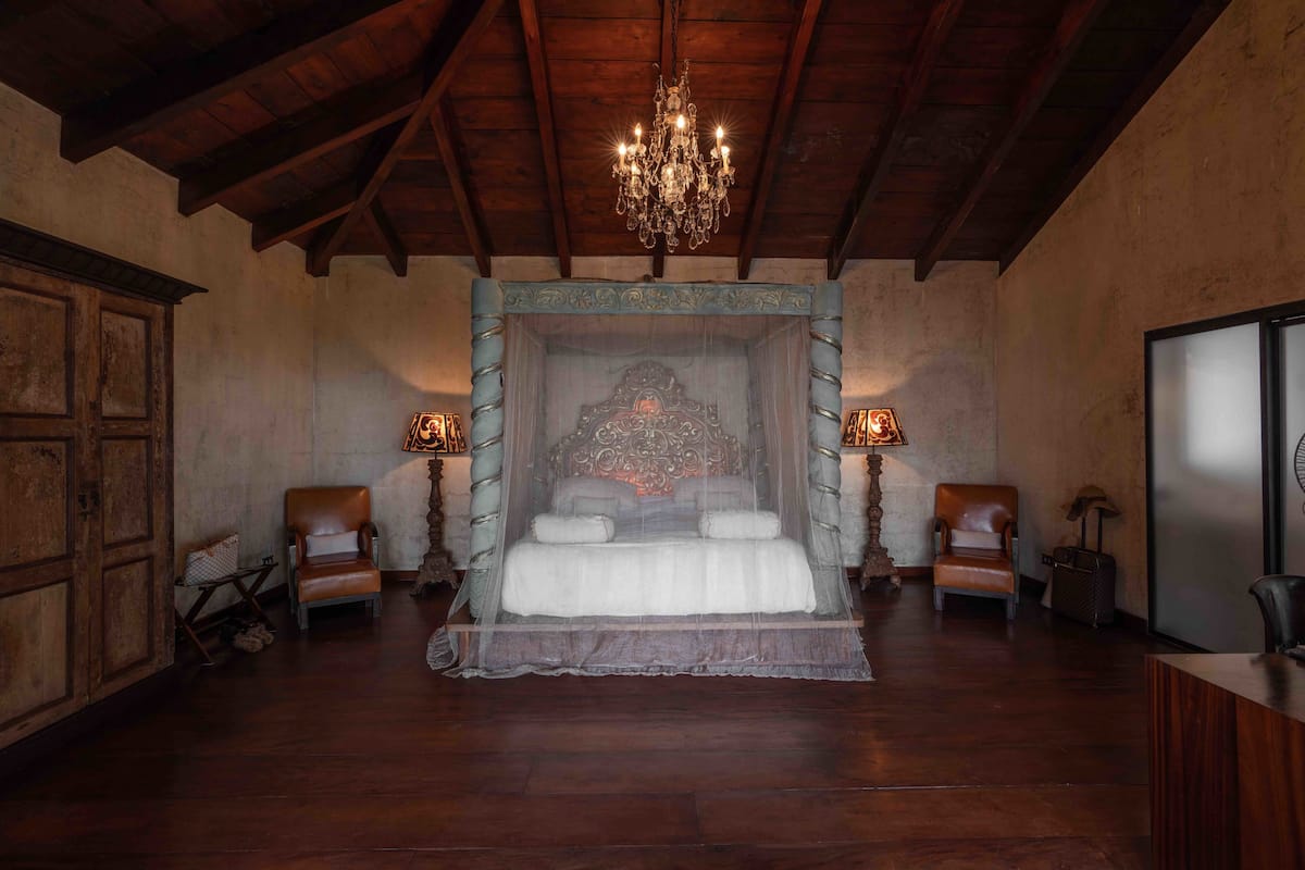 Ein geräumiges Schlafzimmer mit einem großen Bett, Holzbalkendecke, einer Kristallleuchtre und zwei Nachttischen mit Lampen.