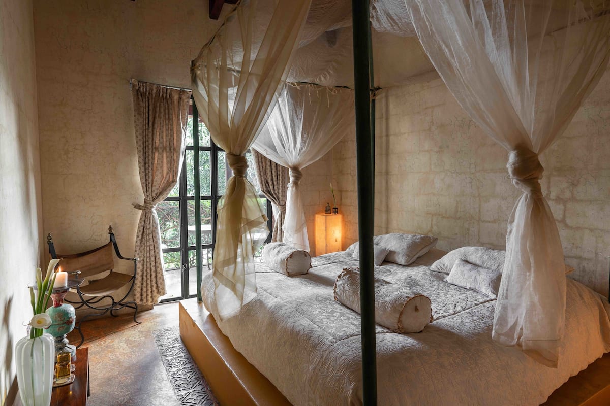 Ein Schlafzimmer mit einem großen Bett, einer Bank, einem Tisch mit Kerzen und einem Fenster mit Vorhängen.