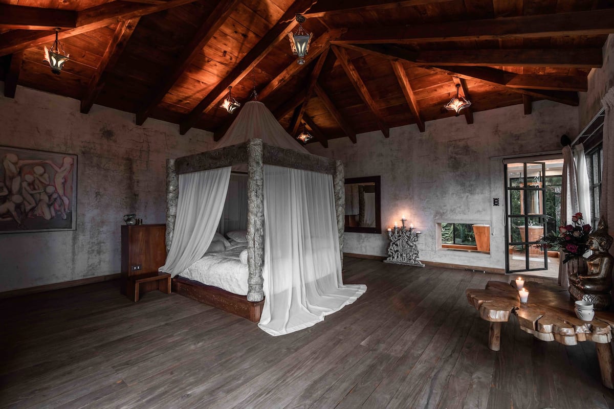 Ein rustikales Schlafzimmer mit einem Himmelbett, Holzbalken und einem großen Fenster mit Blick.