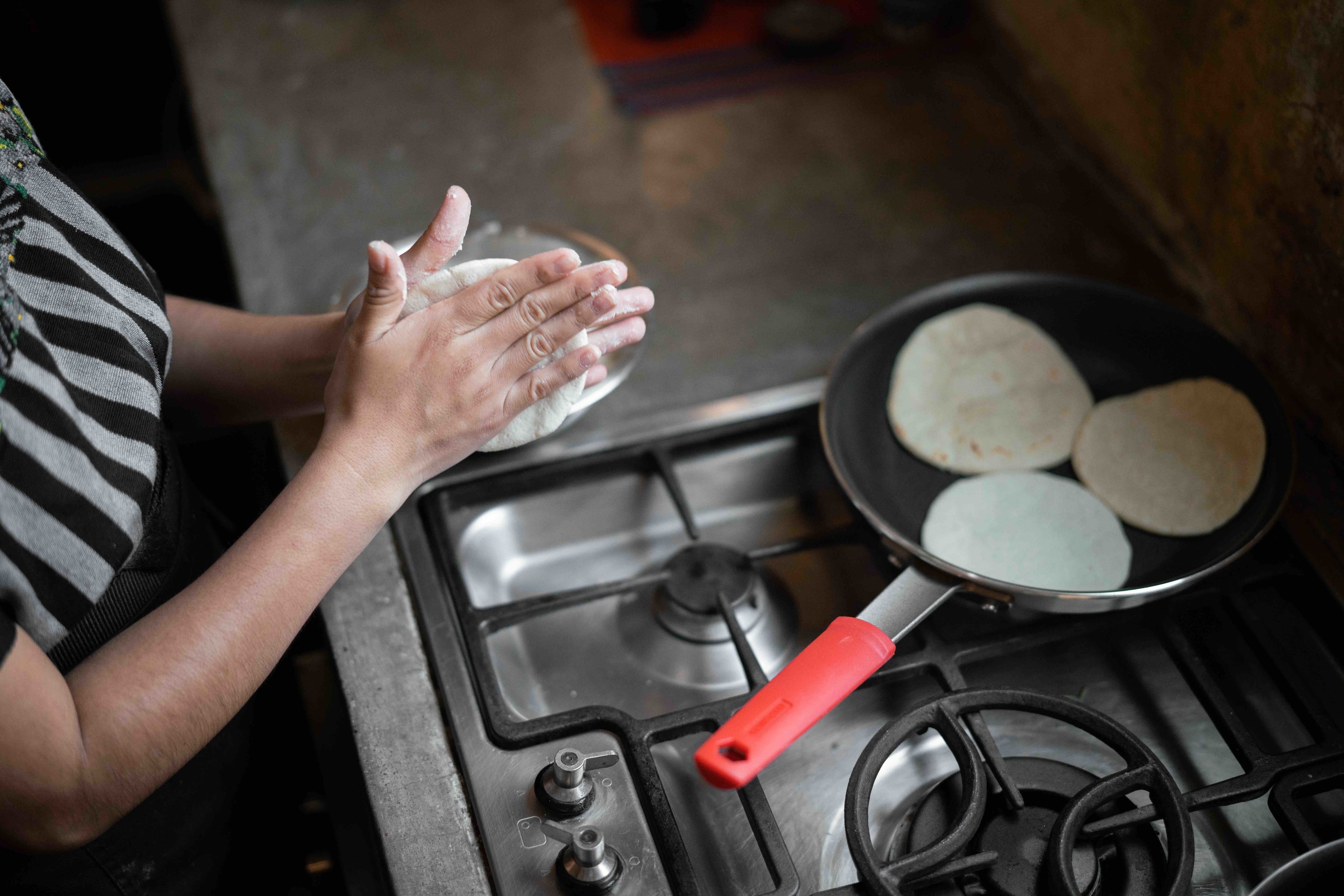 A person cooking tortillas on a stove with a red handle.