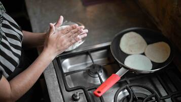 A person cooking tortillas on a stove with a red handle.