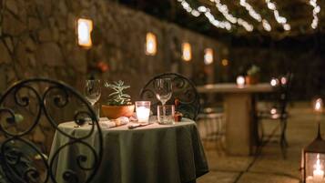 Un área de comedor al aire libre con una mesa preparada para dos personas, que incluye una vela, un vaso y una planta pequeña.