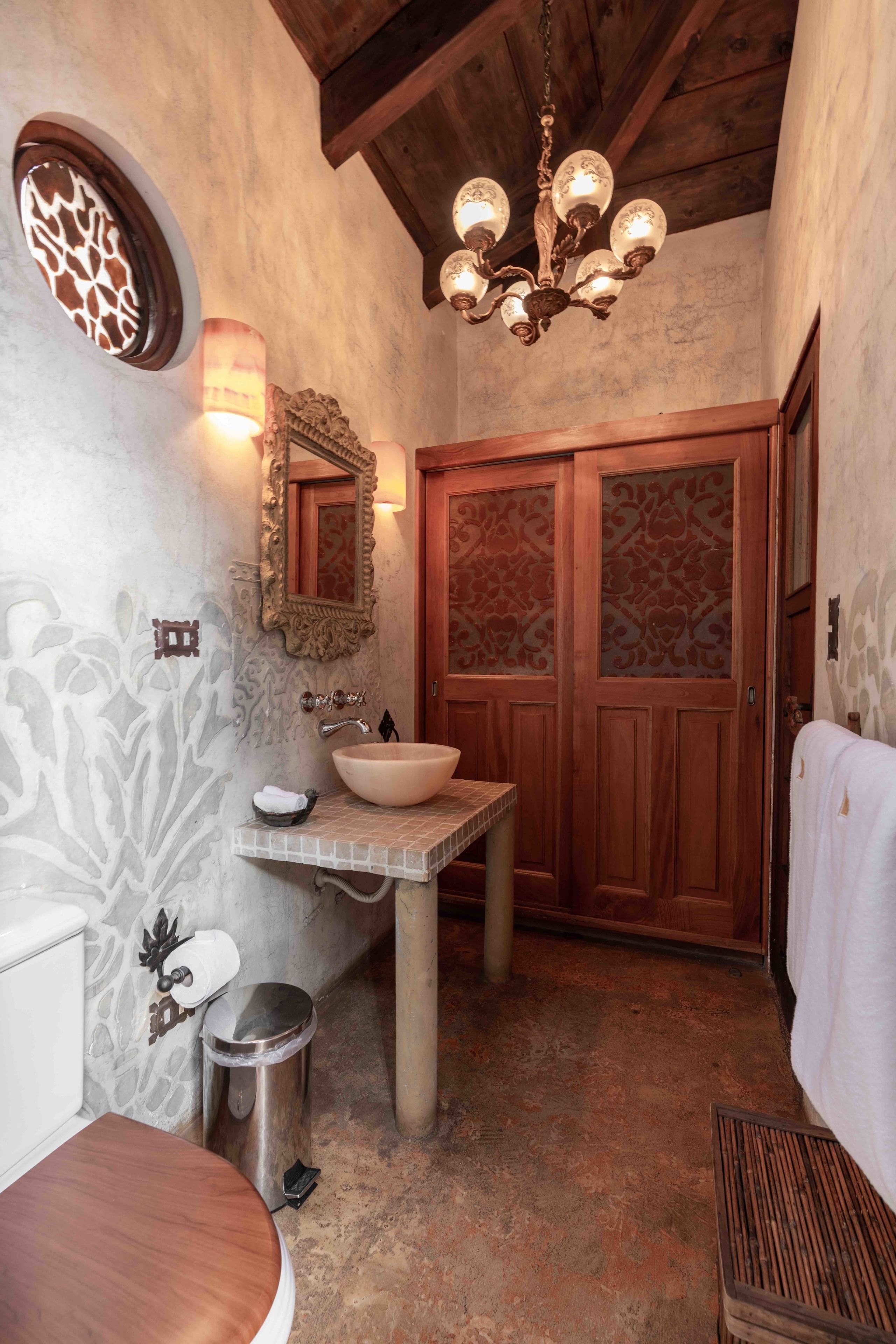 A bathroom with a wooden vanity, a large mirror, a chandelier, and a decorative wall.