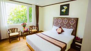 A hotel room with a large bed, two chairs, a small table with a vase of flowers, and a window with curtains. - Hoang Anh 1 Hotel (Hanoi)