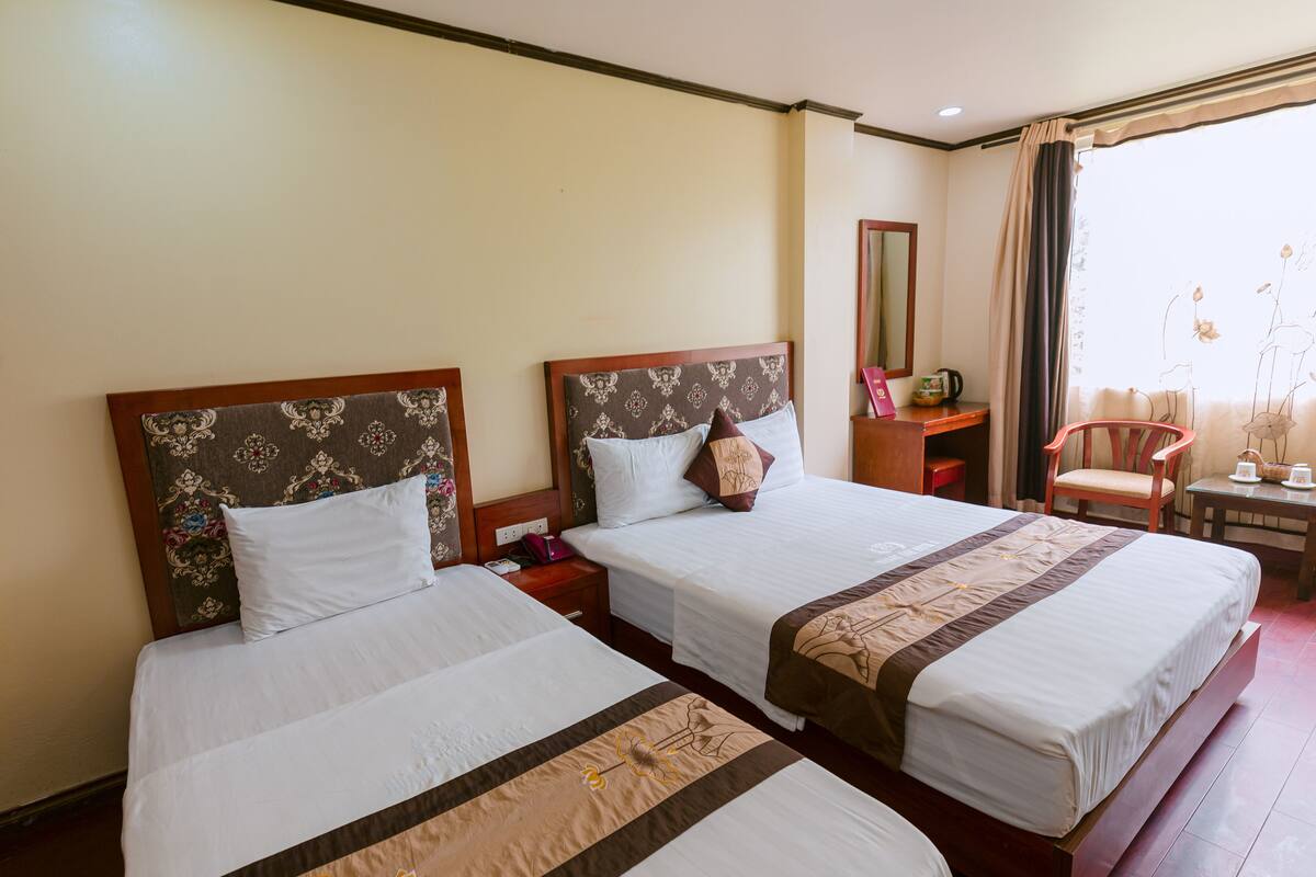 A hotel room with two beds, a desk, a chair, and a window with curtains.