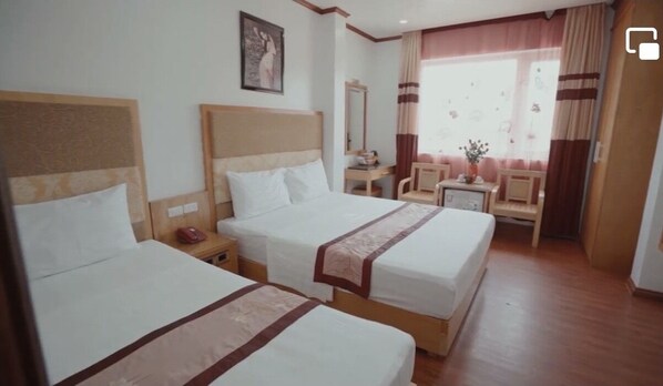 A hotel room with two beds, a desk, a chair, a mirror, and a window with curtains.