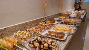 Un bufé con diversos alimentos, incluyendo pasteles, bollería y sándwiches.