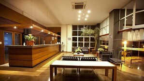 Un área de recepción moderna con un mostrador de madera, zona de estar y grandes ventanales.