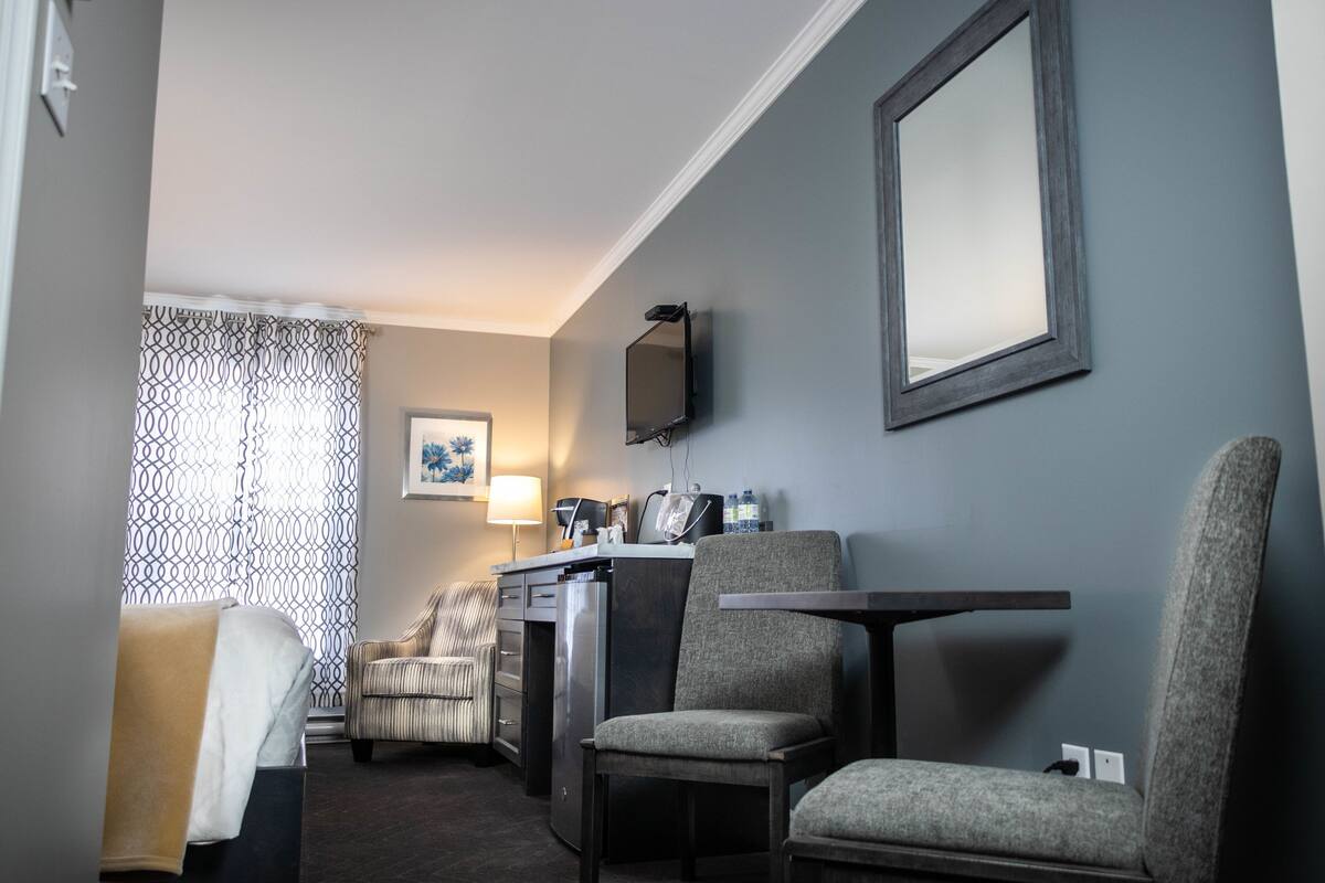 Una habitación de hotel con escritorio, dos sillas, televisor y espejo.