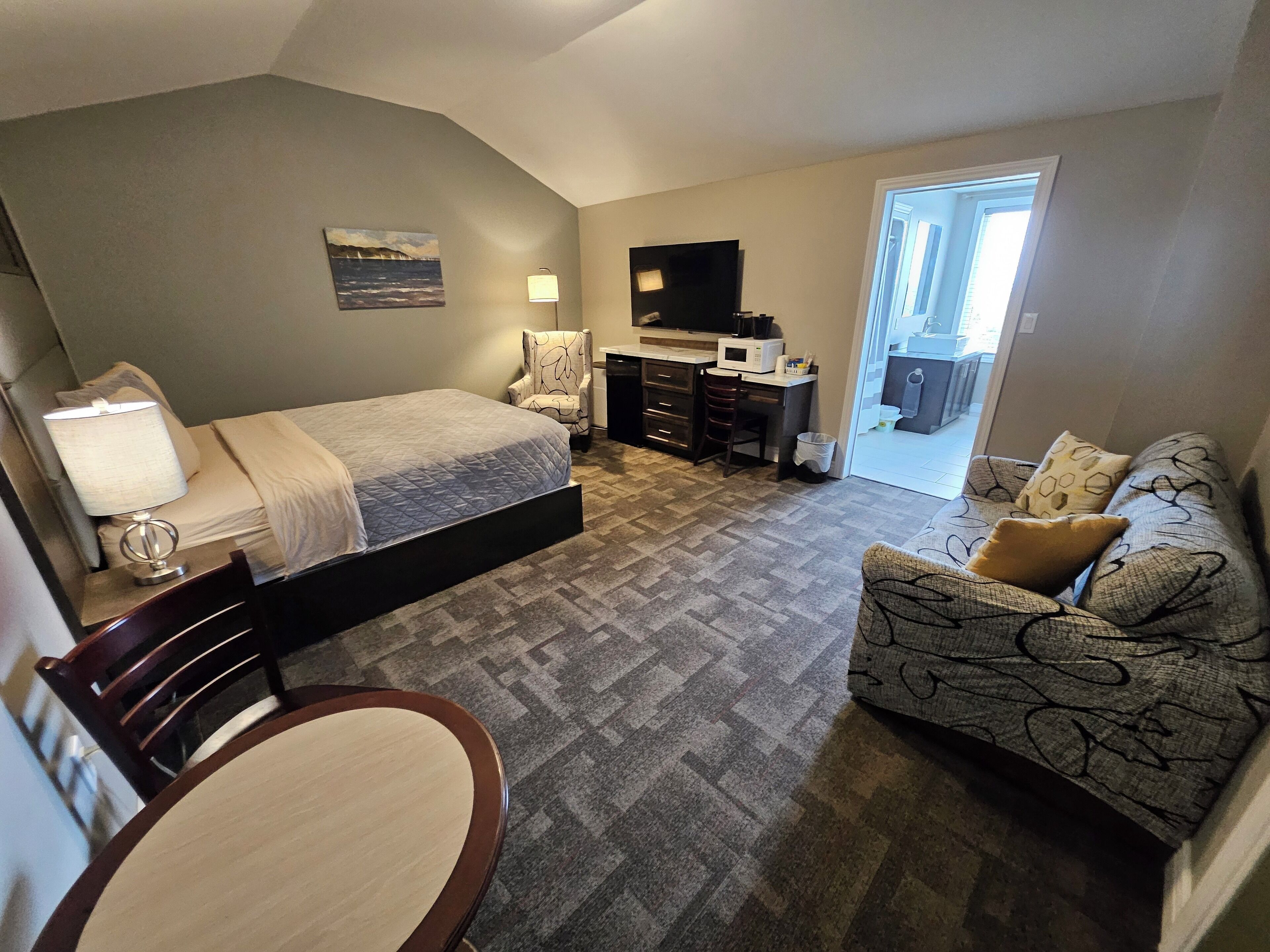 A compact hotel room with a bed, a desk, a chair, a sofa, and a small dining table.