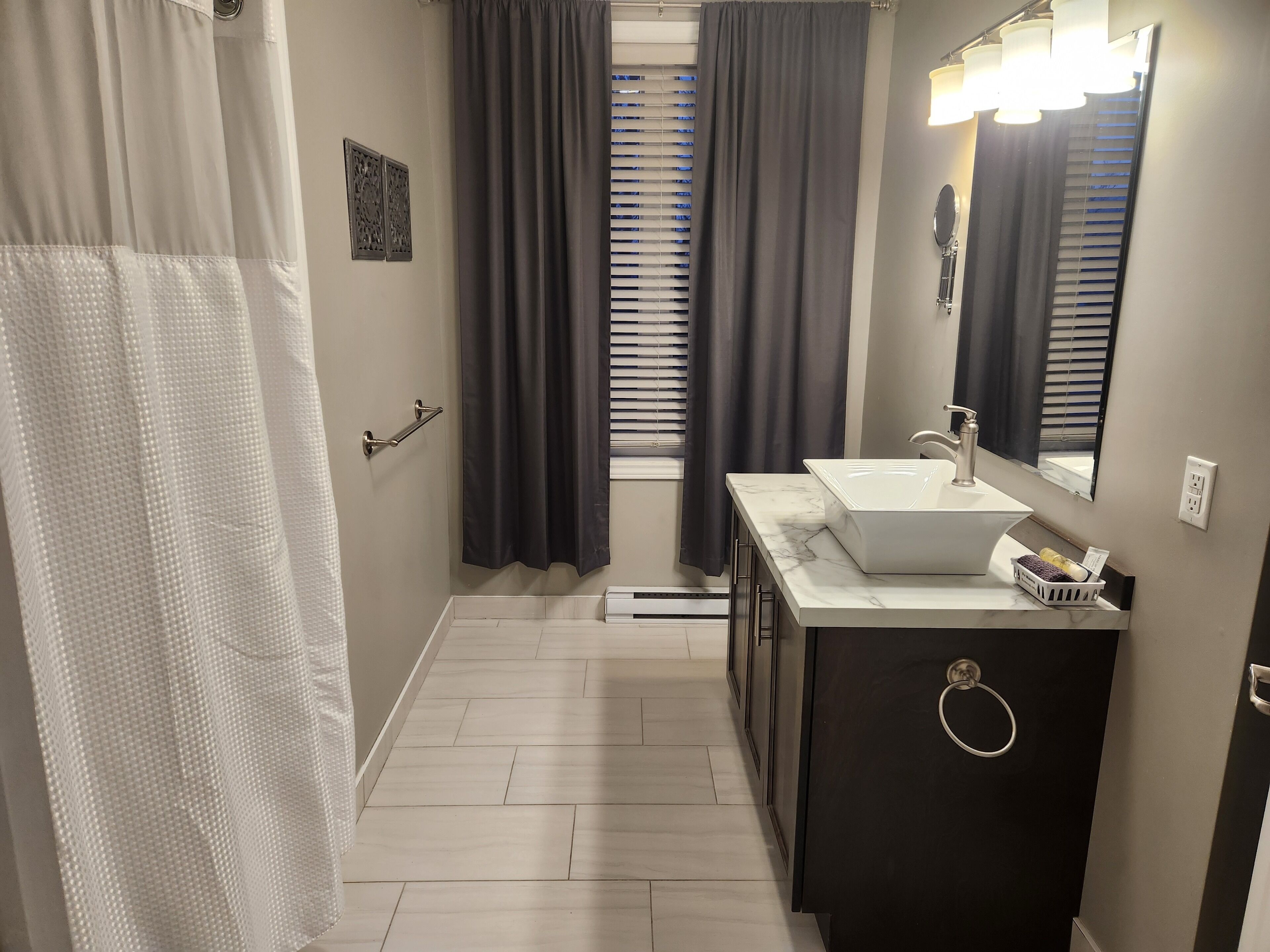 A modern bathroom with a white sink, dark cabinet, and a mirror with lights.