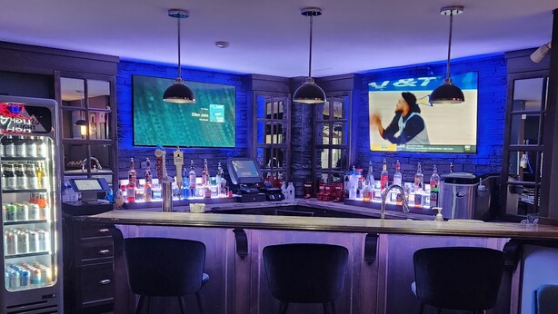 A bar area with a counter, stools, and a large screen displaying a sports event. - Newfound Inn & Suites (Conception Bay South)