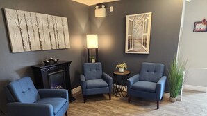 A room with two blue armchairs, a small table with a plant, a fireplace, and wall art. - Newfound Inn & Suites (Conception Bay South)