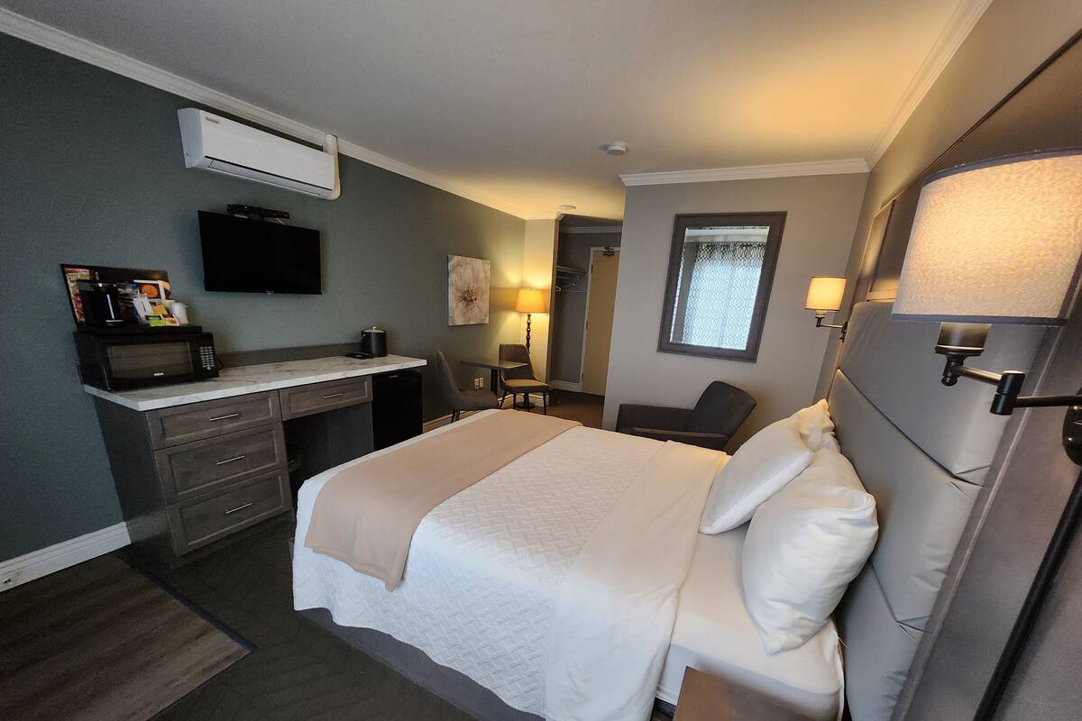 Una habitación de hotel con cama, mesita de noche, escritorio, silla y un equipo de aire acondicionado.
