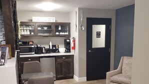 A modern living room with a grey sofa, a dining area with a table and chairs, a kitchen area with appliances and cabinets, and a door with a fire safety sign. - Newfound Inn & Suites (Conception Bay South)
