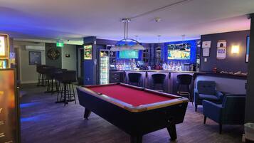 A billiards table in a bar area with a pool table, bar stools, and a dartboard.