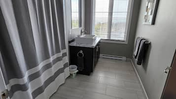 A bathroom with a shower curtain, a sink, a mirror, and a window with blinds.