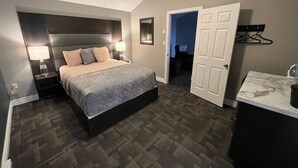 A bedroom with a bed, bedside tables, a nightstand, a dresser, and a walk-in closet. - Newfound Inn & Suites (Conception Bay South)