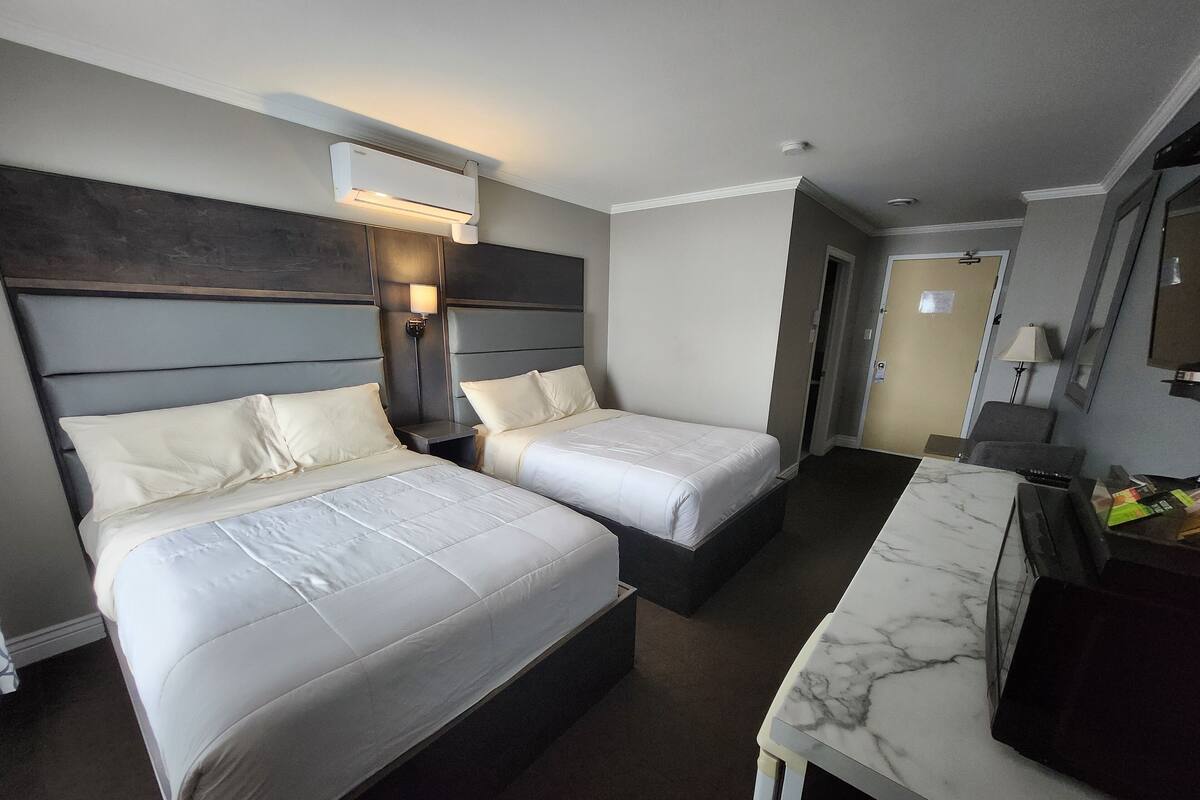 Habitación de hotel con dos camas, un escritorio de superficie de mármol, un aire acondicionado instalado en la pared y una puerta que da a otra habitación.
