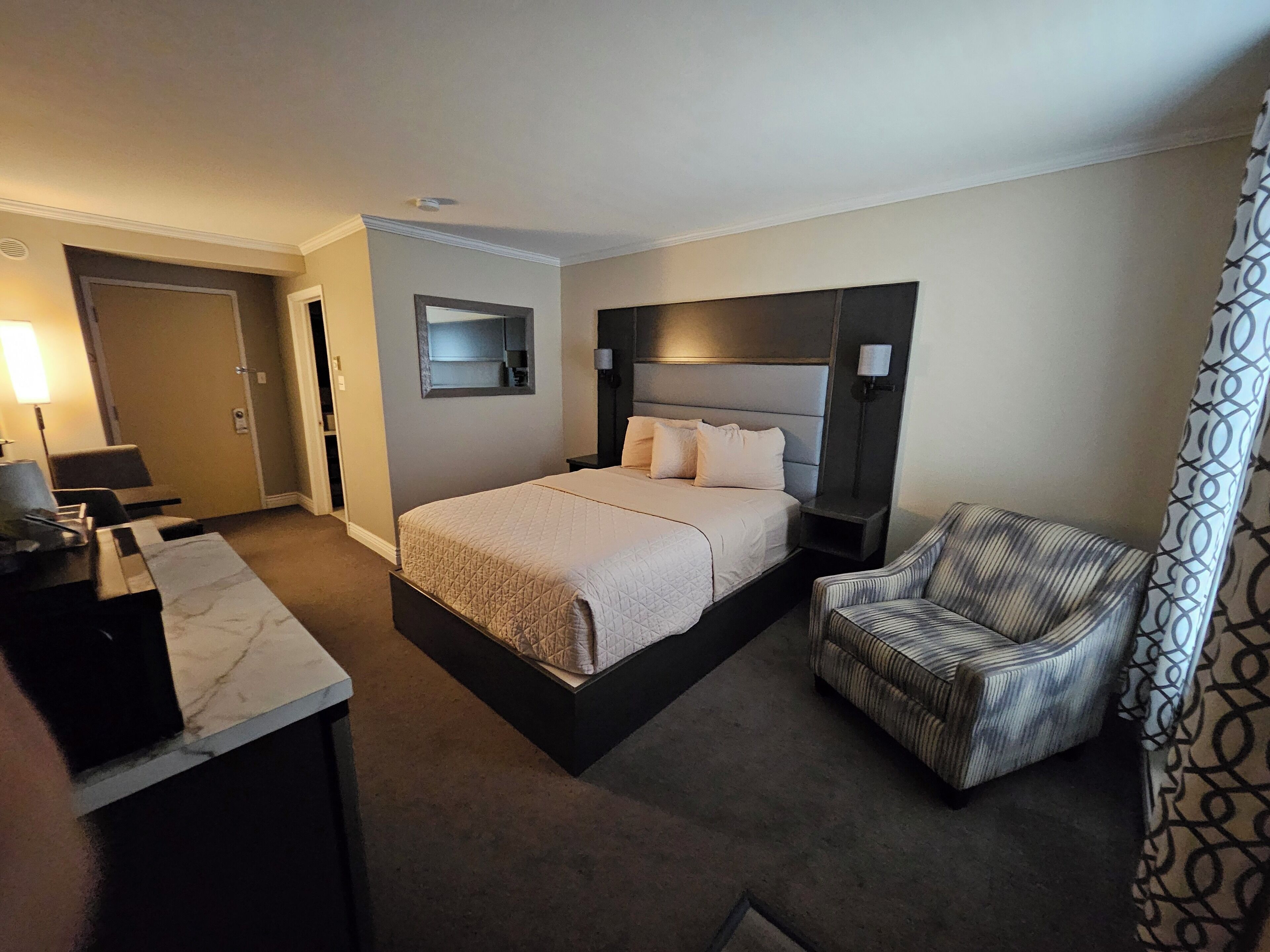 A hotel room with a bed, a desk, a chair, and a mirror.