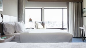 A hotel room with a large bed, a desk, and a chair. There is a window with a view of the city. - Hilton Garden Inn Madison Sun Prairie (Sun Prairie)