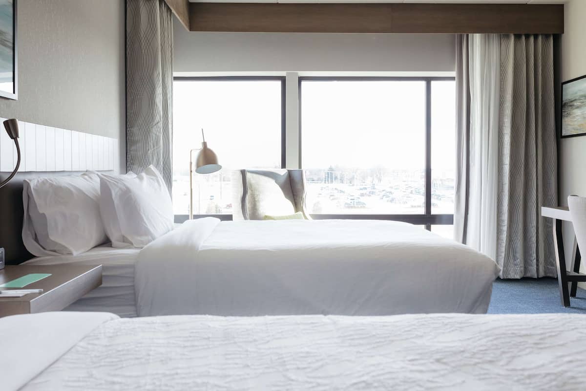 A hotel room with a large bed, a desk, and a chair. There is a window with a view of the city.