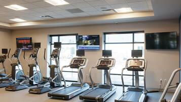 Un gimnasio con cintas de correr, elípticas y una pantalla de televisión mostrando videos de ejercicios.