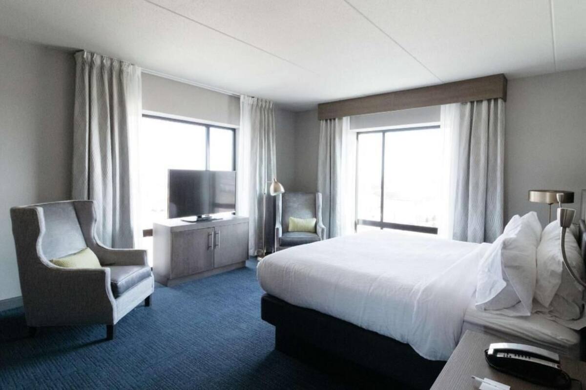 A hotel room with a bed, a TV, a chair, and a desk with a lamp.