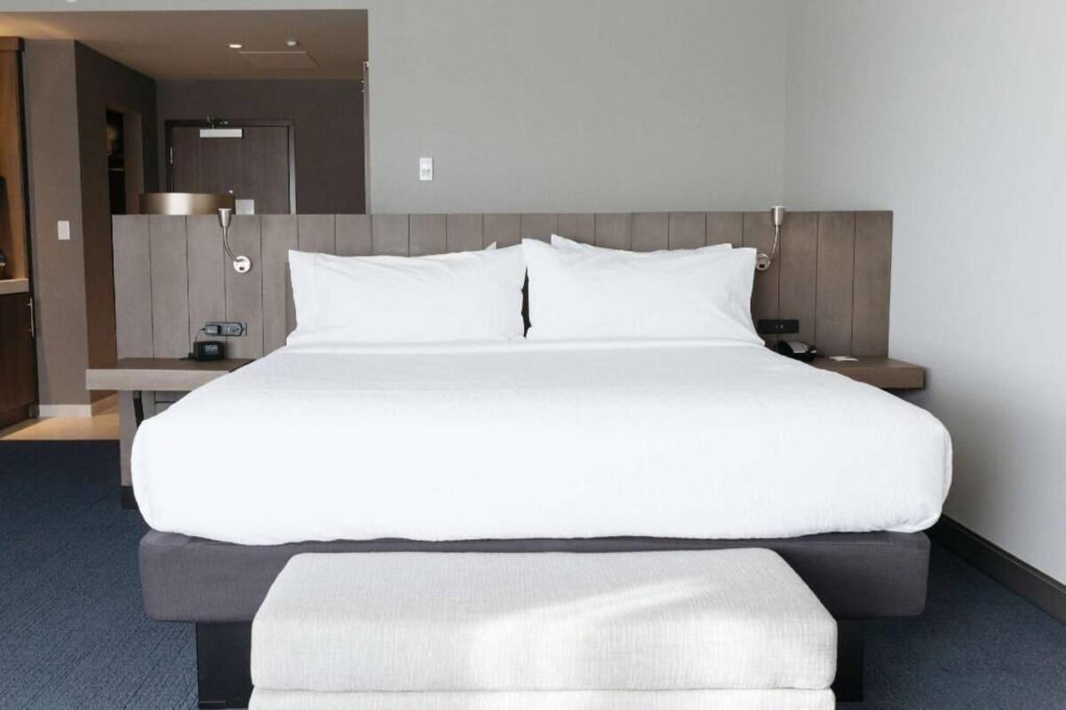 A modern hotel room with a large bed, bedside tables, and a built-in bench.