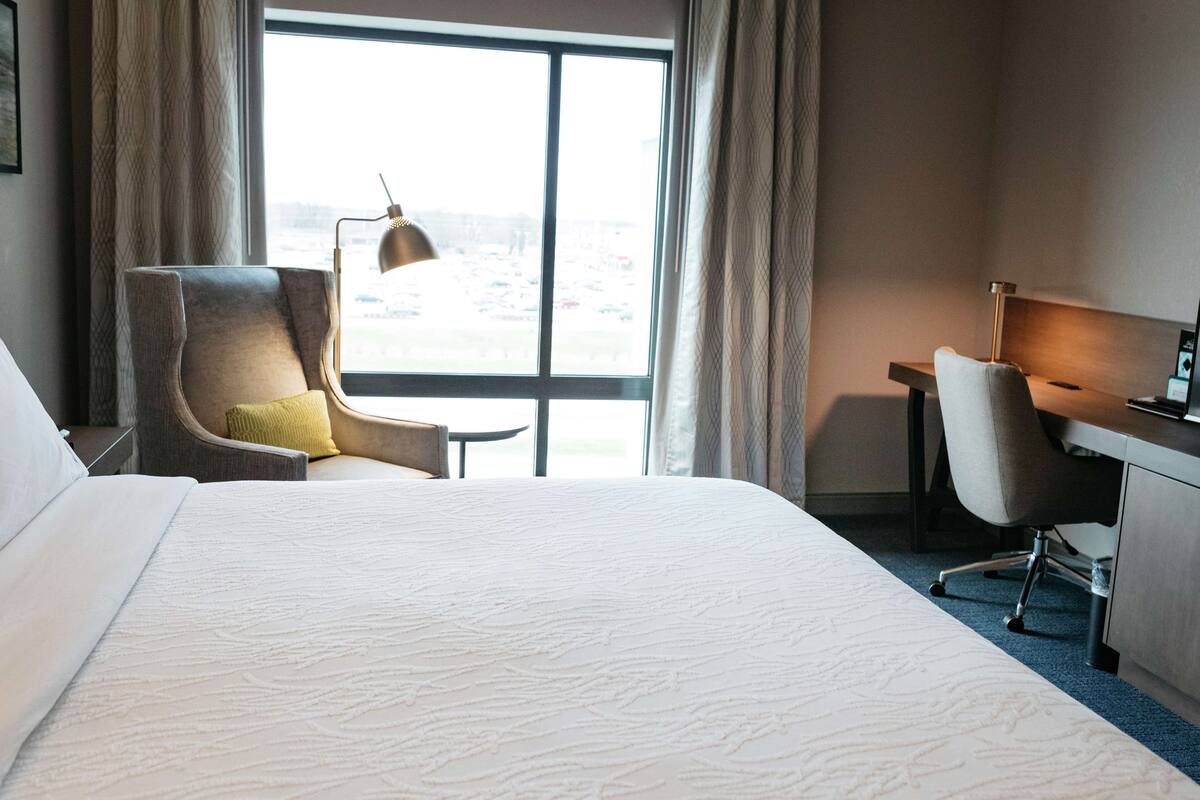 A hotel room with a large bed, a desk, a chair, and a window with curtains.