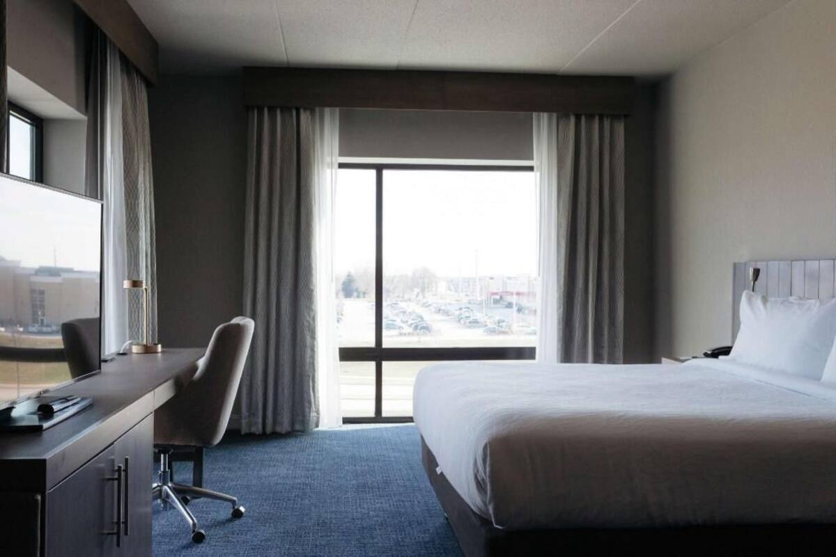 A hotel room with a bed, a desk, a chair, a TV, and a large window with curtains.