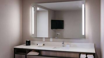 A modern bathroom with a large mirror, a sink, and a television mounted above it.
