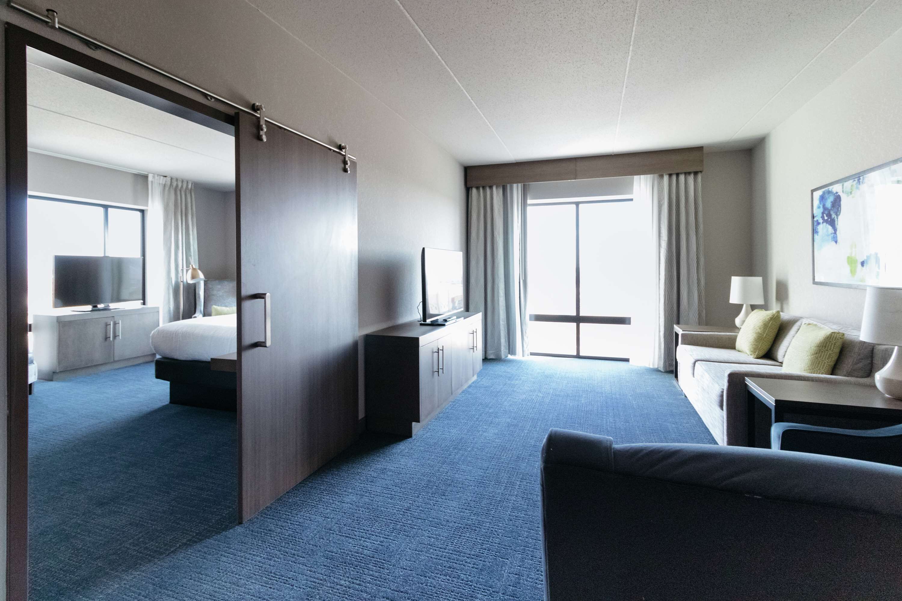 A hotel room with a bed, a desk, a chair, a TV, and a large window.