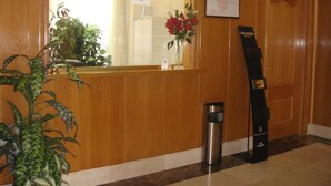 A reception area with a wooden reception desk, a potted plant, a framed certificate, and a trash bin. - Hostal Serpol (Palencia)
