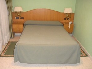 A single bed with a wooden headboard, two bedside tables with lamps, a telephone, and a green bedspread. - Hostal Serpol (Palencia)