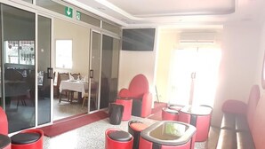 A modern lounge area with red and black seating, a glass partition, and a dining area visible through the partition.