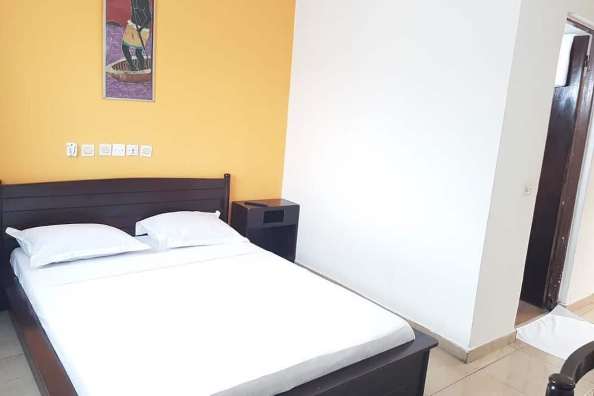 Un dormitorio con una cama, una mesita de noche, un estante en la pared y una puerta.