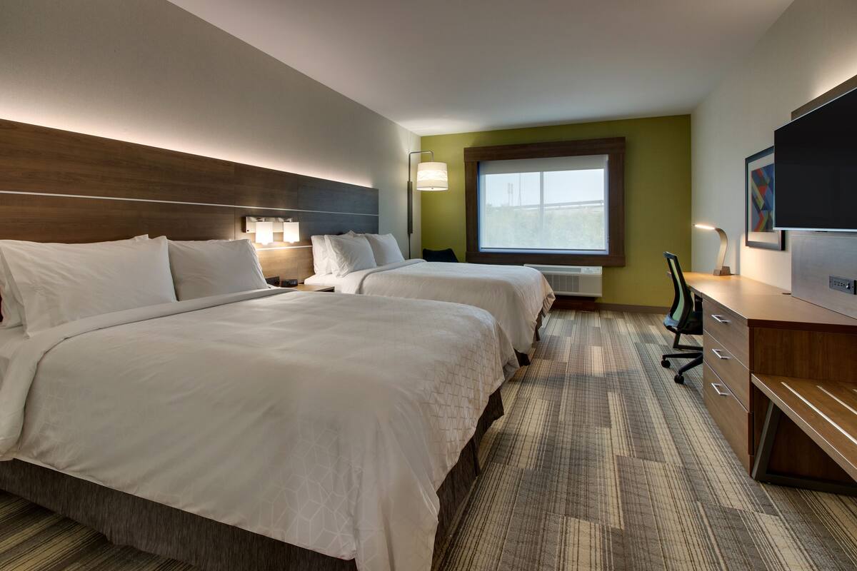 A hotel room with two beds, a desk, a chair, and a TV.