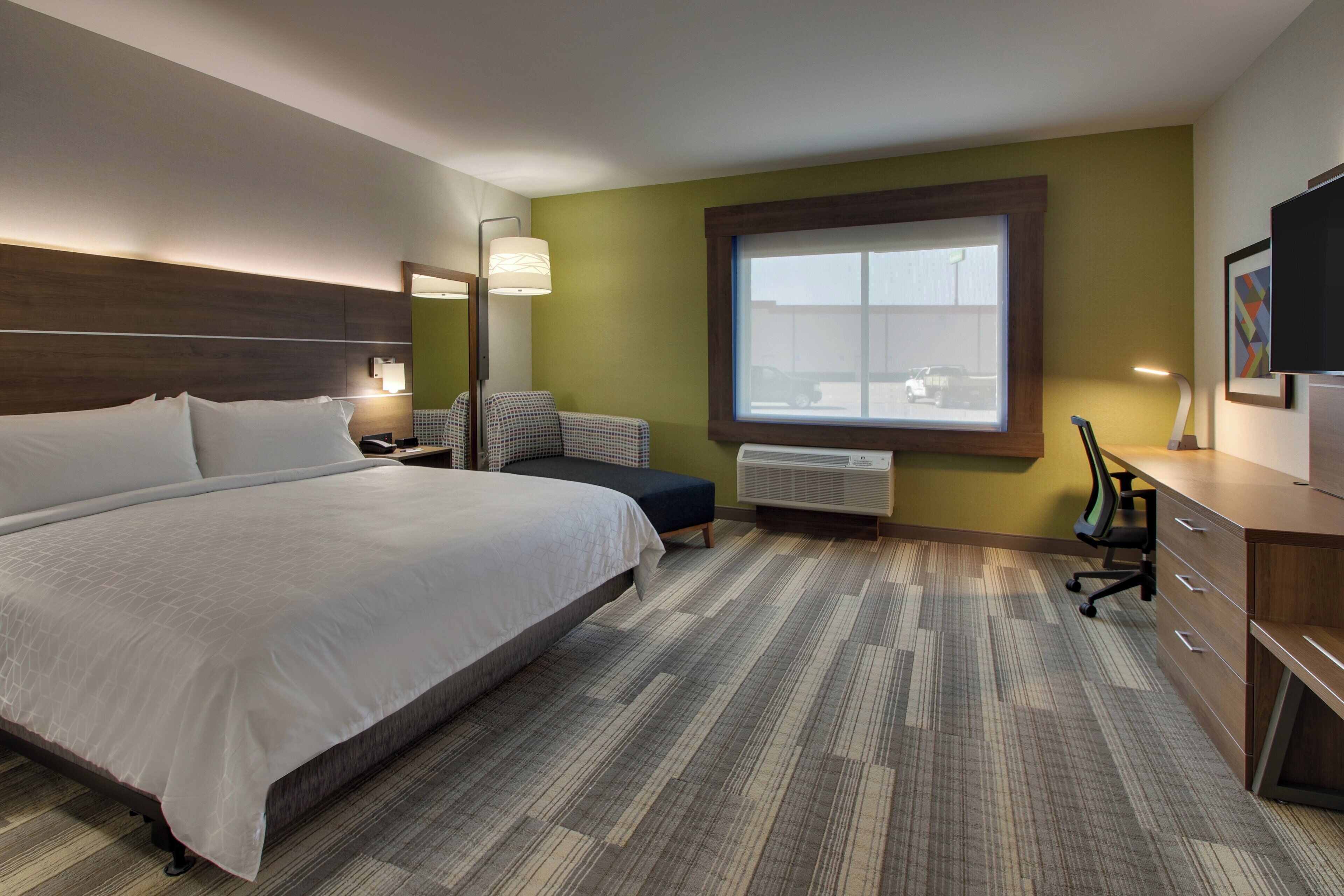Une chambre d’hôtel avec un grand lit, un bureau, une chaise, une fenêtre et un téléviseur.