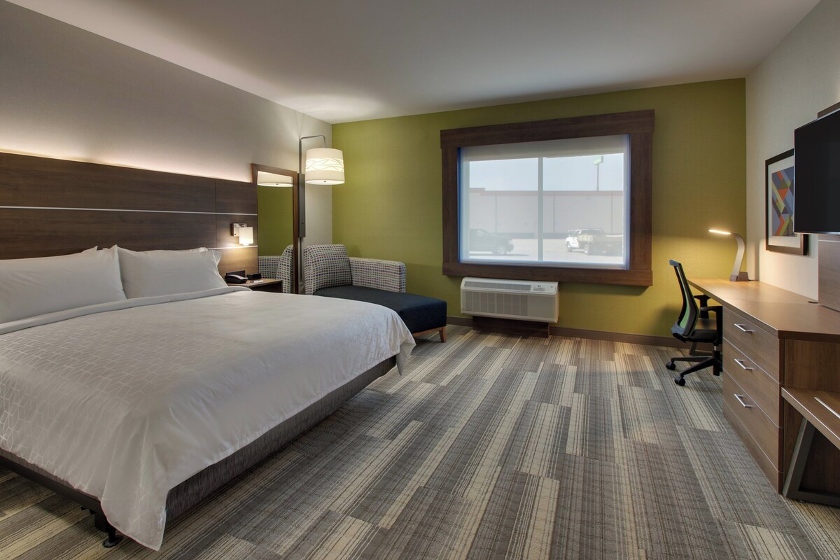 Ein Hotelzimmer mit einem großen Bett, einem Schreibtisch, einem Sessel, einem Fenster und einem Fernseher.