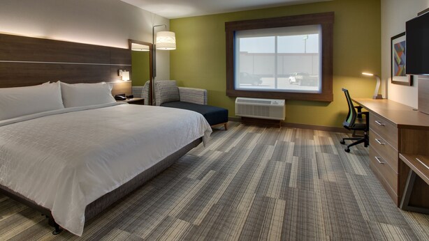 Ein Hotelzimmer mit einem großen Bett, einem Schreibtisch mit Stuhl, einem Fenster mit Blick nach draußen und einem am Wand befestigten Fernseher.