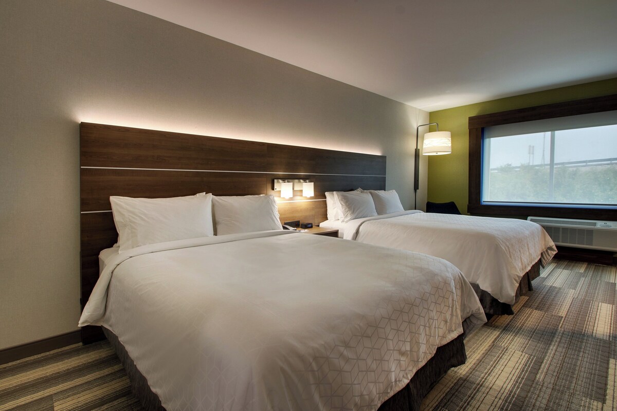 Ein Hotelzimmer mit zwei Betten, einem Nachttisch, einer Lampe und einem großen Fenster.