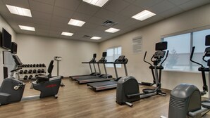 Ein Fitnessstudio mit Laufbändern, Crosstrainern und einem Gewichtesständer.