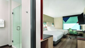 Habitación de hotel con cabina de ducha de vidrio, dos camas, un escritorio y una silla.
