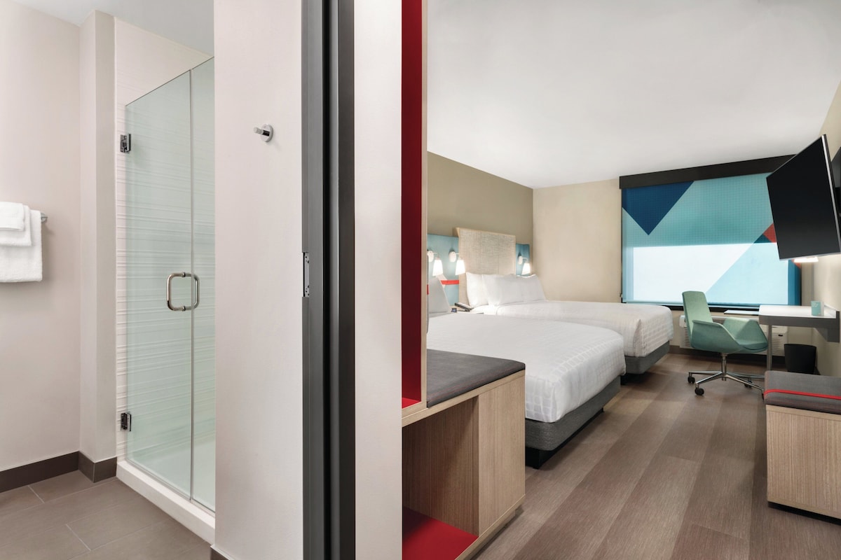 Een hotelkamer met douche, bed, bureau en televisie.