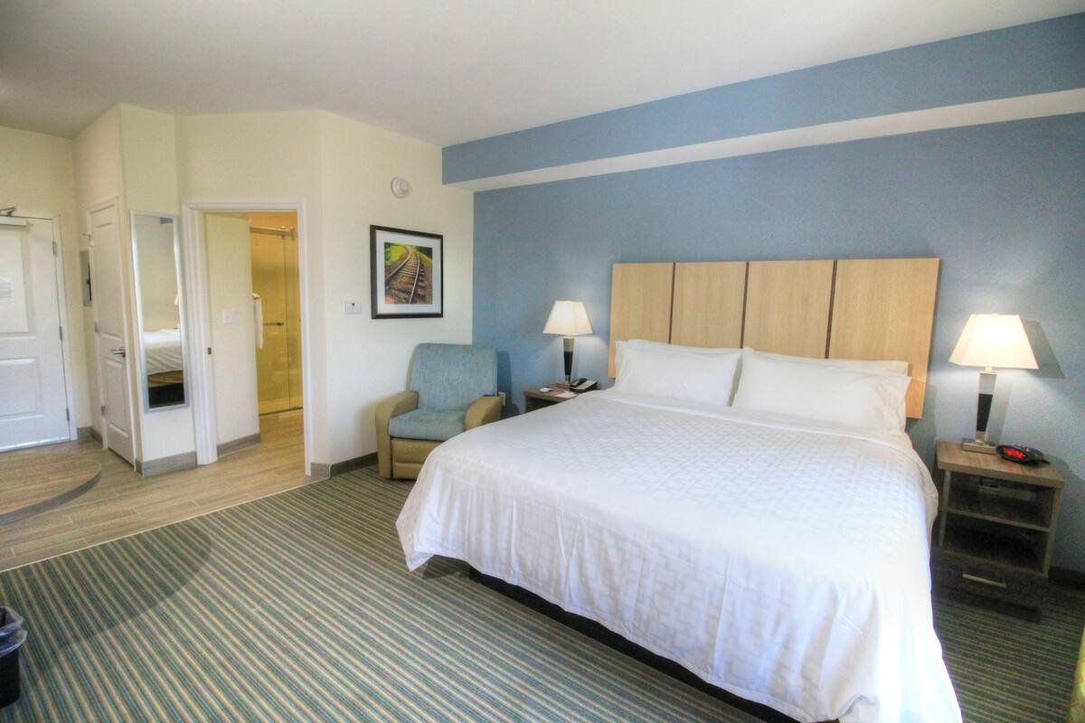 Une chambre d’hôtel comprenant un lit, deux lampes de chevet, une chaise, une table de chevet et une porte donnant sur une autre pièce.