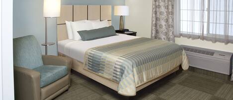 Hotelkamer met een bed, een stoel, twee bedlampen, een raam met gordijnen en een airconditioning.