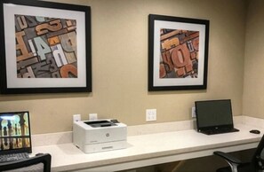 Un espace de travail comprenant deux œuvres d’art abstraites encadrées, une imprimante de bureau, un ordinateur portable et un écran affichant une vue urbaine.