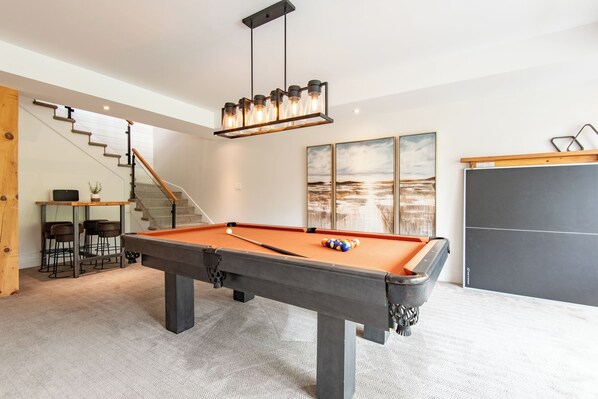 A pool table in a modern room with a staircase, a bar area, and artwork on the wall. - Havre Ride-Out | Ski-in/out | 4300 sq.ft Luxury Townhouse | Hot Tub & Semi-Private Yard & Shuttle (Mont-Tremblant)