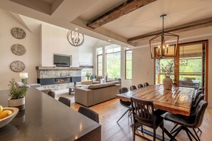 A spacious living area with a fireplace, comfortable seating, a large wooden dining table, and a television mounted on the wall. - Havre Ride-Out | Ski-in/out | 4300 sq.ft Luxury Townhouse | Hot Tub & Semi-Private Yard & Shuttle (Mont-Tremblant)